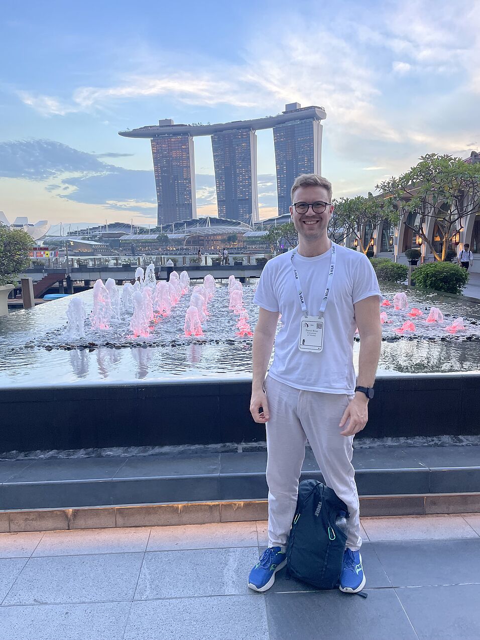Young man with glasses, standing in front of a fountain in Singapore.